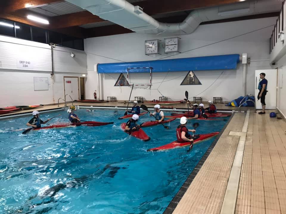 Canoe polo players practising in an indoor swimming pool.