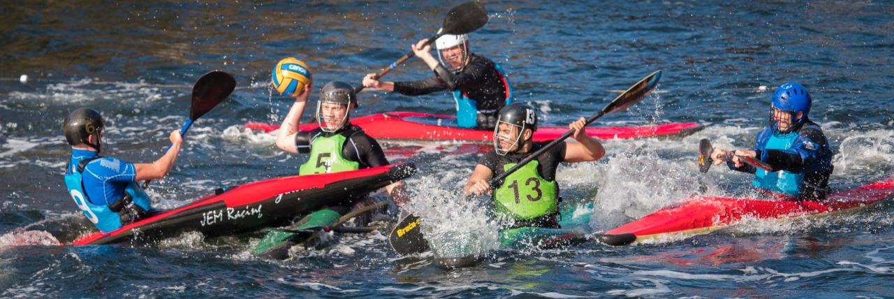 Canoe polo players in green and blue buoyancy aids competing for the ball.